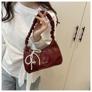 Close-up of deep red crescent bag with pleated handle and pearl bow charm accessory