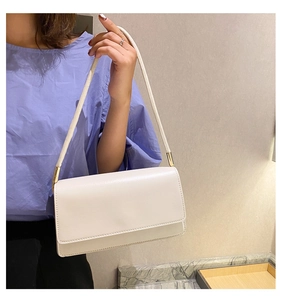 Minimalist white leather underarm bag with gold metal hardware on model shoulder