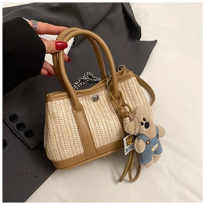 Detail of woven straw handbag with brown leather trim and cute teddy bear charm