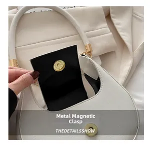 Detailed view of the gold magnetic snap closure on a white crescent bag.