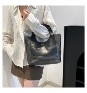Detail of vintage straw tote bag with black leather stitching and sleek metal buckle closure