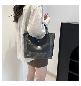 Close-up of contrast stitching on woven tote bag with leather flap and metal buckle