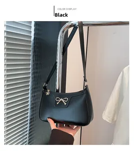 Détail du sac baguette noir avec boucle nœud dorée et pendentif fleur au zip