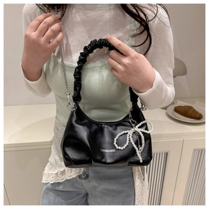 Detail of a black crescent bag featuring pleated shoulder straps and a pearl bow charm