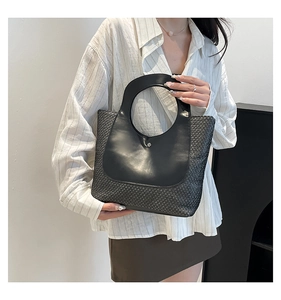 Detail of round cutout handle and metallic buckle on black woven straw handbag