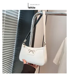 Détail du sac baguette blanc avec nœud métallique sur texture cuir matifié