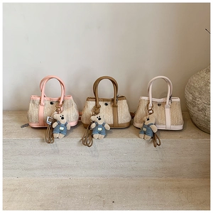 Three straw tote bags with colorful PU trims and cute bear charms on stone steps