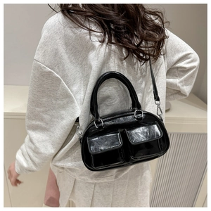 Detail of a black patent leather crossbody bag with dual pockets and glossy oil-wax finish