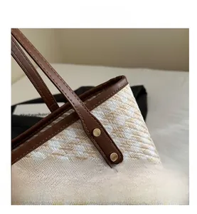 Detail of woven tote bag with brown leather handles and golden rivet hardware