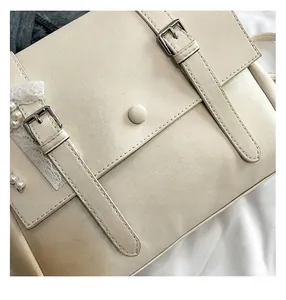 Close-up detail of cream white faux leather handbag with buckle straps and lace accent