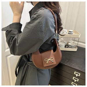 Brown crescent underarm bag with gold bow detail worn by a model in a stylish interior