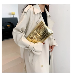 Close-up of golden envelope clutch featuring crocodile pattern and large square metal buckle