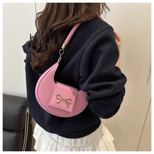 Model wearing a stylish pink crescent-shaped shoulder bag with a gold bow detail