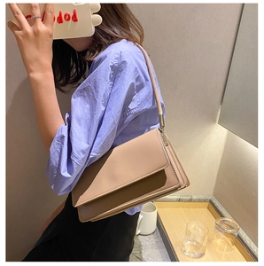 Close-up of minimalist beige leather underarm bag worn by a model in a casual blue shirt