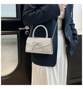 Détail du mini sac argenté brillant avec nœud et chaîne en métal sur une robe blanche