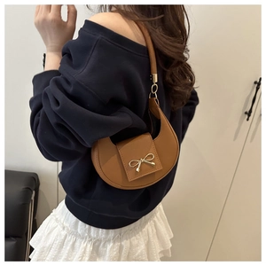 Close-up detail of a stylish brown crescent-shaped underarm bag with a golden bow