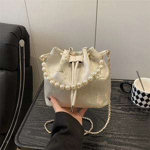 Elegant cream bucket bag with pearl handle and bamboo embroidery in a lifestyle setting