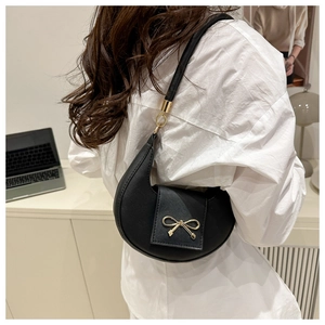 Detailed side view of a black crescent hobo bag with a gold bow-knot on a model.