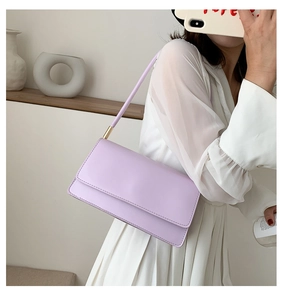 Detail of lavender leather shoulder bag with gold hardware worn by a model in minimalist setting