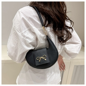 Close-up of a black crescent underarm bag with a golden bow decoration on a model