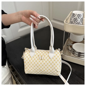Close-up of white cylindrical Boston bag with yellow floral prints and butterfly buckle