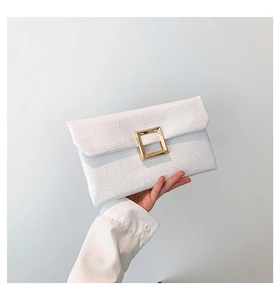 Macro detail of white crocodile-embossed envelope clutch bag with gold metallic buckle