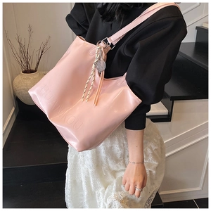 Detail of pink leather tote bag featuring embossed logo and braided charm on handle