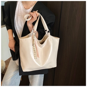 Detail of white glossy tote bag with texture, letter embossing and braided charm