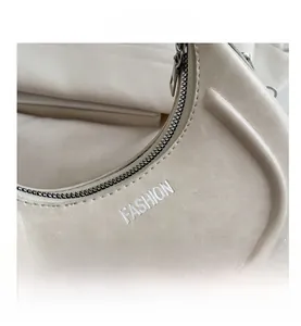 Dettaglio macro della borsa a mezzaluna beige con zip argento e ricamo FASHION bianco