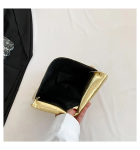 Detail of golden envelope clutch with crocodile texture showing zipper and black lining