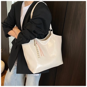 Detail of a creamy white glossy tote bag with embossed logo and tassel on a female model