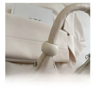 Dettaglio della borsa beige che mostra la trama della pelle e il manico con perline
