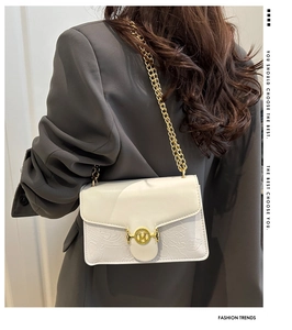 Detail of white embossed floral shoulder bag with gold chain strap and metal logo