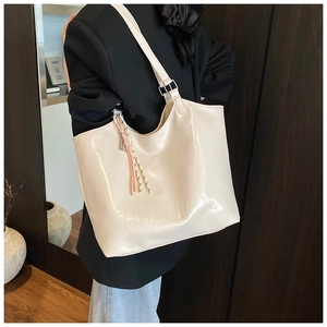 Detail of cream glossy tote bag featuring embossed logo and a braided tassel charm