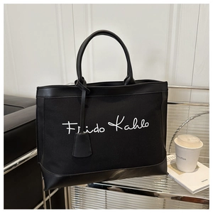 Gros plan d'un sac cabas en toile noire avec broderie de la signature Frida Kahlo