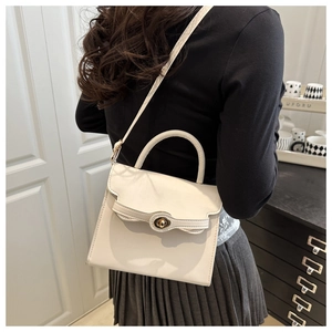 Cream white crossbody bag detail showing the golden oval twist lock and handle on model