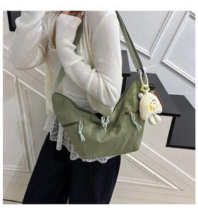 Detailed view of grass green crescent crossbody bag with white plush charm on model