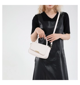 Detalle de bolso minimalista crema en cuero sintético con elegante barra dorada