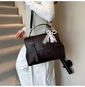 Sac bandoulière vintage en cuir marron foncé avec un nœud décoratif en dentelle et perles.