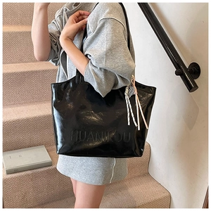 Detail of black glossy tote bag with embossed letters and stylish tassel charm