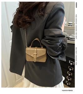 Detail of olive green handbag featuring metal belt buckle and delicate gold chain strap