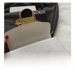 Detail of white embossed leather bag featuring lotus patterns and gold magnetic snap