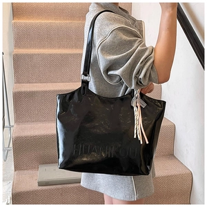 Detail of black patent leather tote bag with embossed logo and decorative tassel