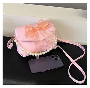 Rosa Umhängetasche mit Schleife und Perlenkette neben Handy für Größenvergleich