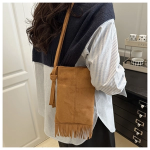 Detail of bohemian warm brown suede crossbody bag with decorative fringe and long strap