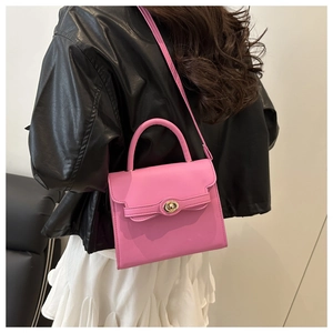 Pink matte leather crossbody bag with gold metallic twist lock on black leather jacket