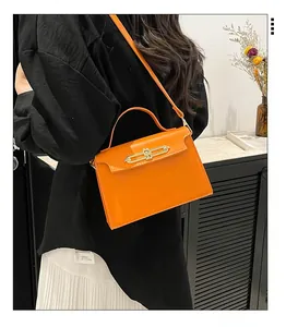 Detail of a bright orange leather handbag with premium gold chain buckle and structured handle