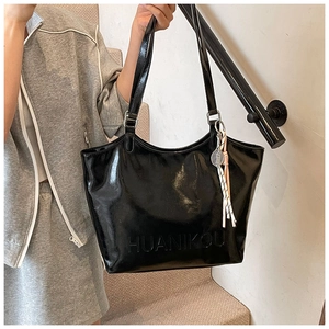 Detail of glossy black tote bag with embossed logo and a creative tennis racket charm