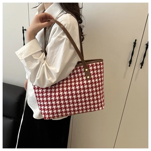 Detail of red and white houndstooth woven tote bag with brown leather straps and gold rivets