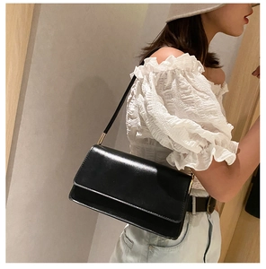 Detail view of a black glossy underarm bag featuring elegant gold metal hardware